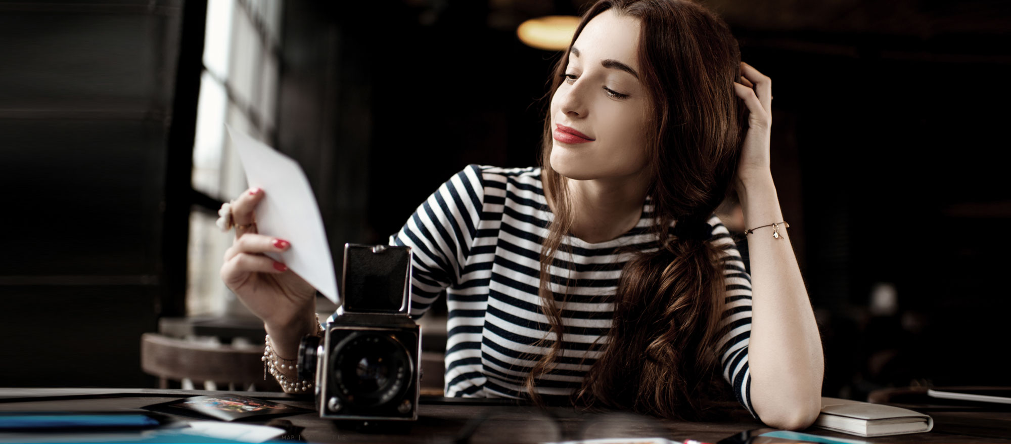 women wearing black and white stripped shirt, red lipstick. Sitting a in dark cafe with her vintage camera, admiring a photo 