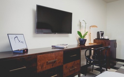 sleek dark wood dresser attached to desk with chair. Above a mounted tv. Next to mini fridge and coffee maker