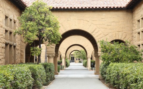 arched pathway of large stone building flanked by green bushes and trees