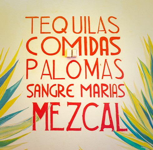 Painted wall mural that says tequilas comidas palomas sangre marias mezcal in red