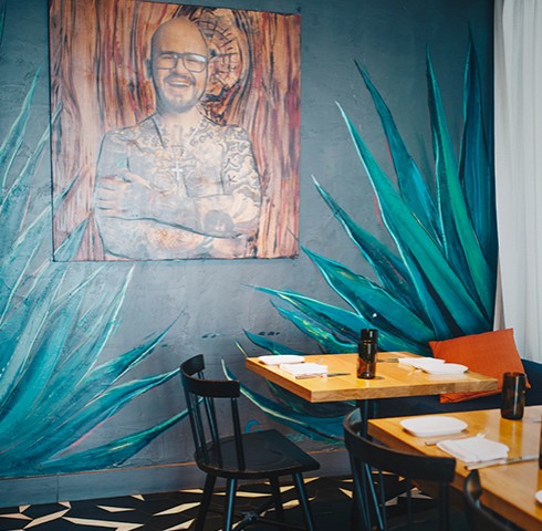 Painted wall mural of agave plants and chef painting with a few tables and chairs