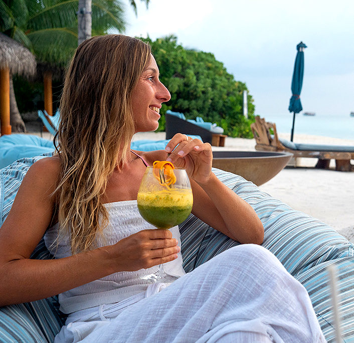 A woman sitting next to the beach and drinking a tropical beverage