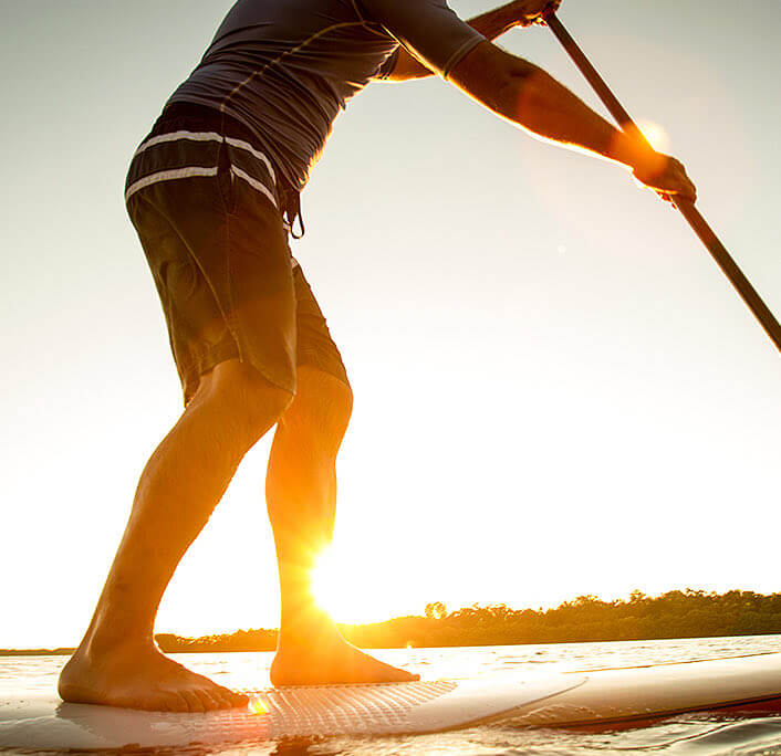 A man at the sea standing up at a paddle board