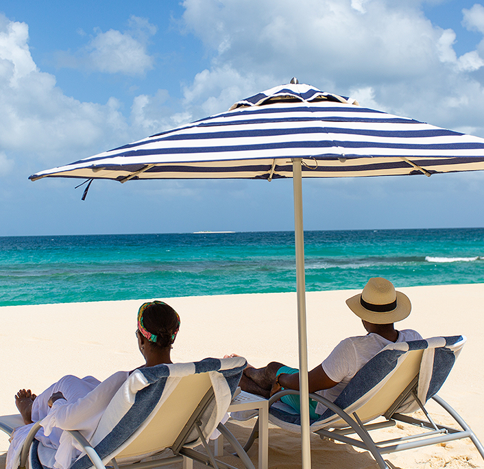A couple sitting on beach chairs under an umbrella enjoying the seaview next to the beach