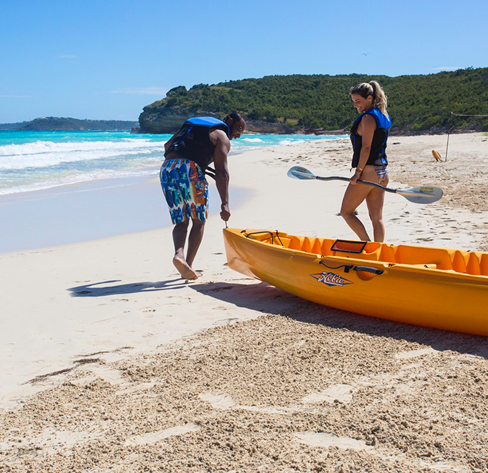 A man carrying a kayak alongside a woman next to the beach