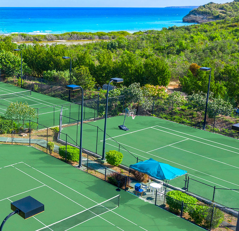 Aerial view of three tennis courts, green threes and the sea at the background