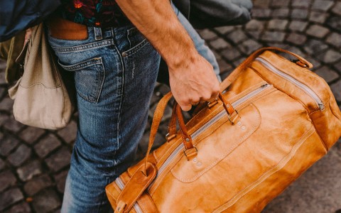 a man walking with a brown leather duffel bag