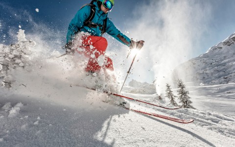 person in a blue coat and red snow pants skiing down a mountain