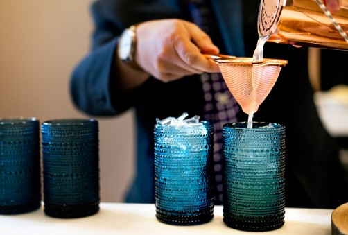 well dressed bartender pouring a beverage through a strainer into a blue cup