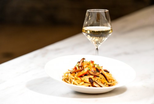 pasta dish served on a white plate with a glass of white wine