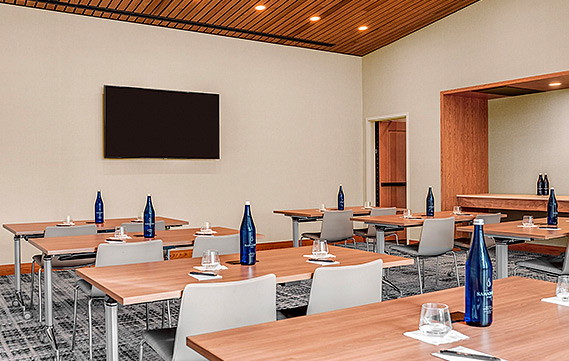 a spacious meeting room with several wooden tables facing a tv on the wall