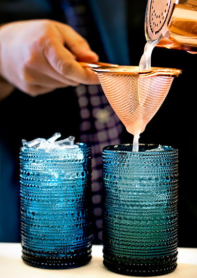 a bartender pouring a drink through a strainer into a blue cup