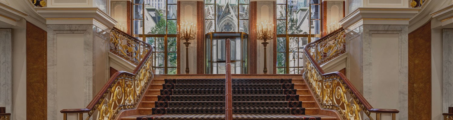 Flight of wooden stairs with golden accents on railing & marble columns on either side