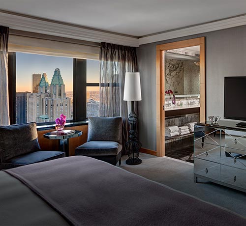Room with bed, glass dresser & chairs by city view window