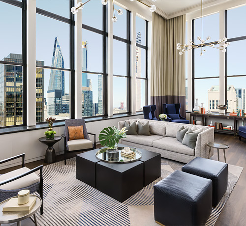 large living room with beige couch and accent chairs and windows overlooking the city
