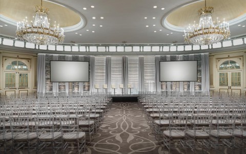 large event space with rows of chairs facing a gray projector screen