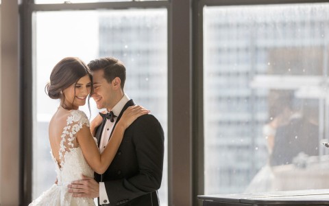 newlyweds hugging in front of large window
