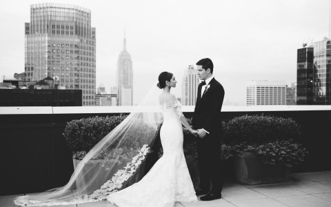 bride and groom pose on the rooftop over looking the city 