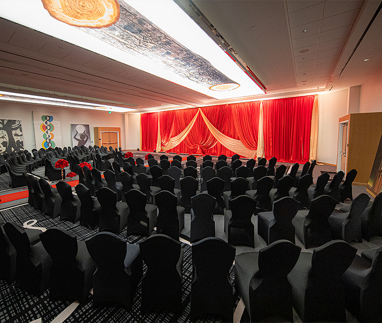 side angle of the ballroom event venue with red drapes on stage and chairs set in front of the stage