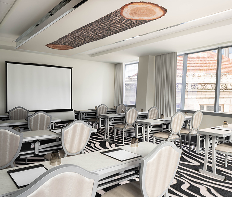Meetings room,  a centered projector screen, with multiple white long tables, chairs and black and white carpet 