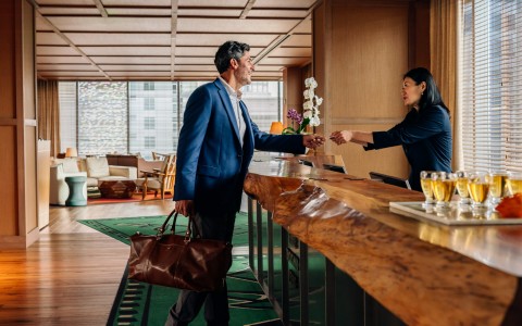 man checking into hotel being greeted and given room key by woman at reception area
