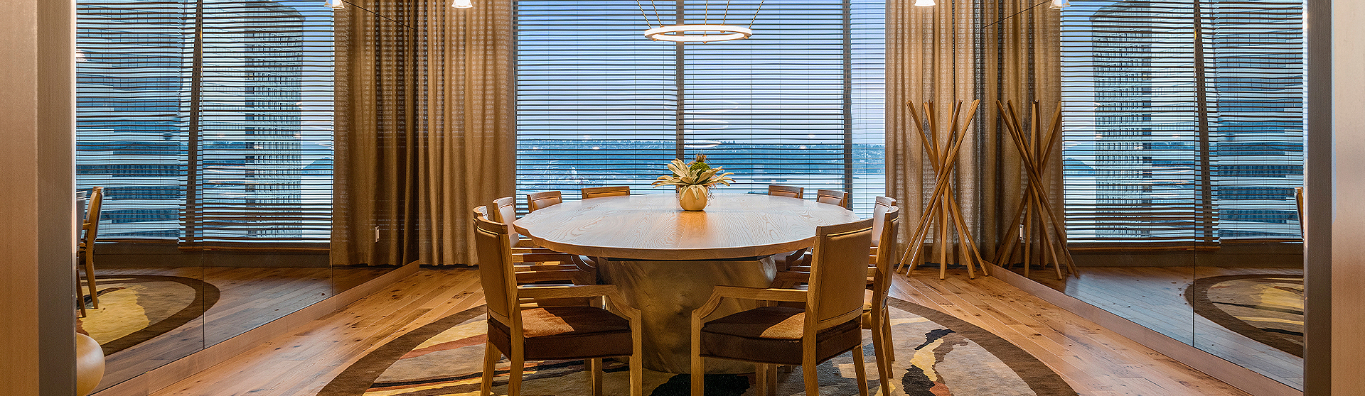 a wooden-vibe room with a table to seat 8 in the center of the room, with large windows behind