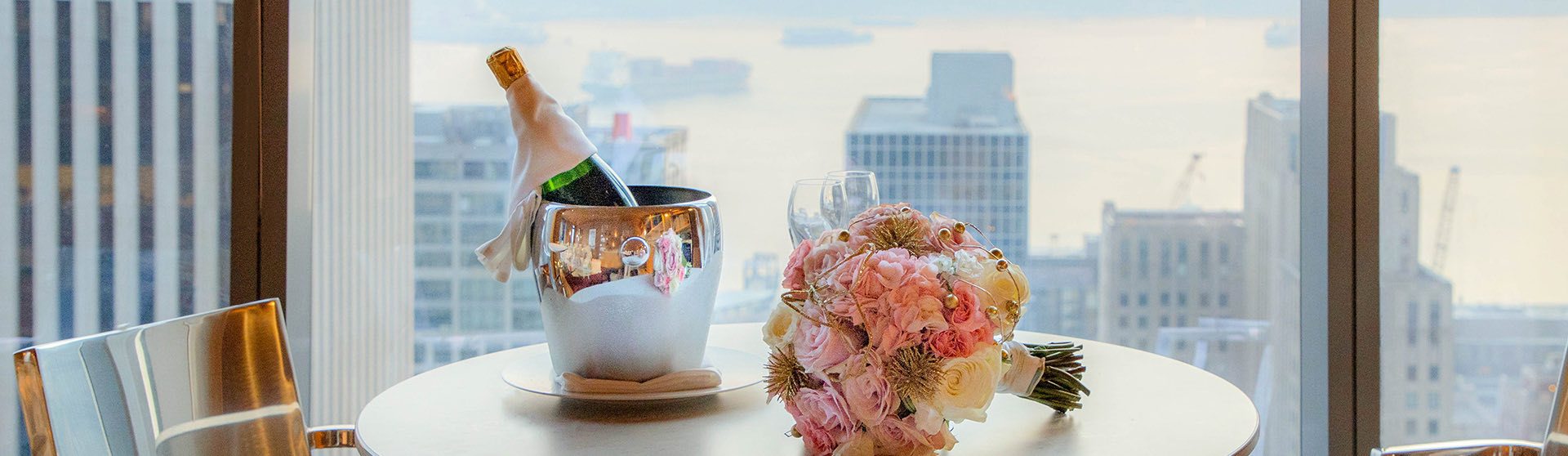bouquet of flowers and a bottle of chilled champagne on the table with the view of the city in the background