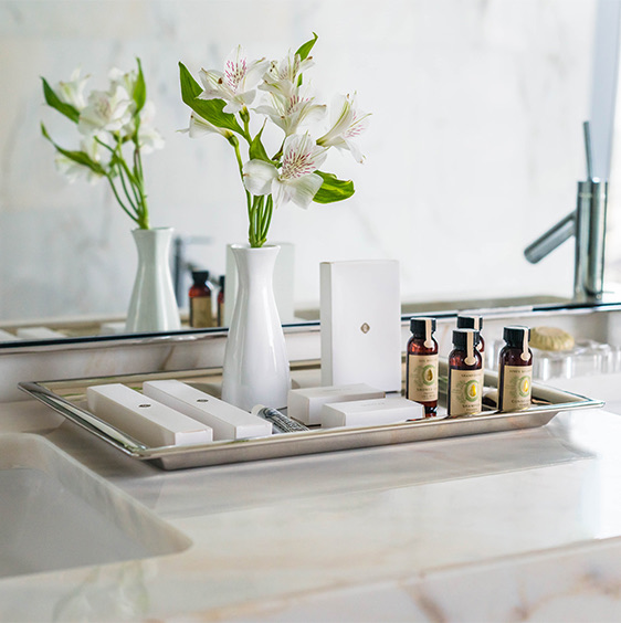 Products and small white vase displayed on silver tray in a marble bathroom