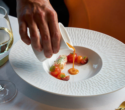 a white plate with tomatoes and a hand pouring a sauce over the tomatoes