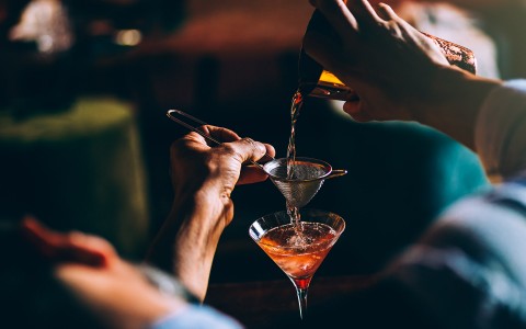 close up of a bartender pouring a cocktail into a glass