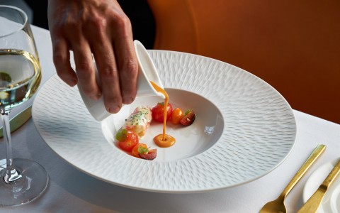 a hand pouring tomato soup in a white bowl