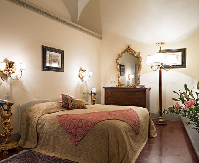 bedroom with beige quilt and red blanket on bed and three lamps
