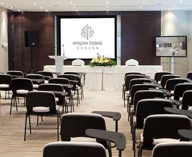 rows of chairs facing a long white cloth covered table with flowers on it and a screen with EMPIRE HOTELS right behind it
