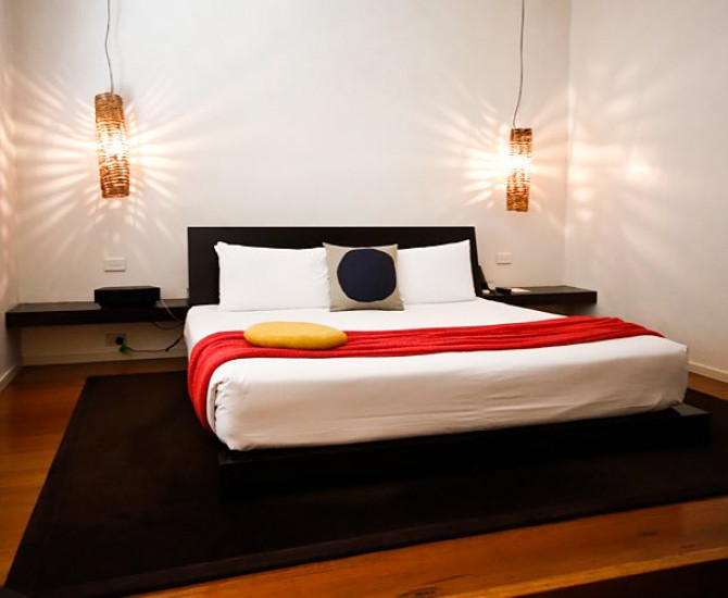 wooden floor with a black carpet underneath a white bed and a red blanket over it