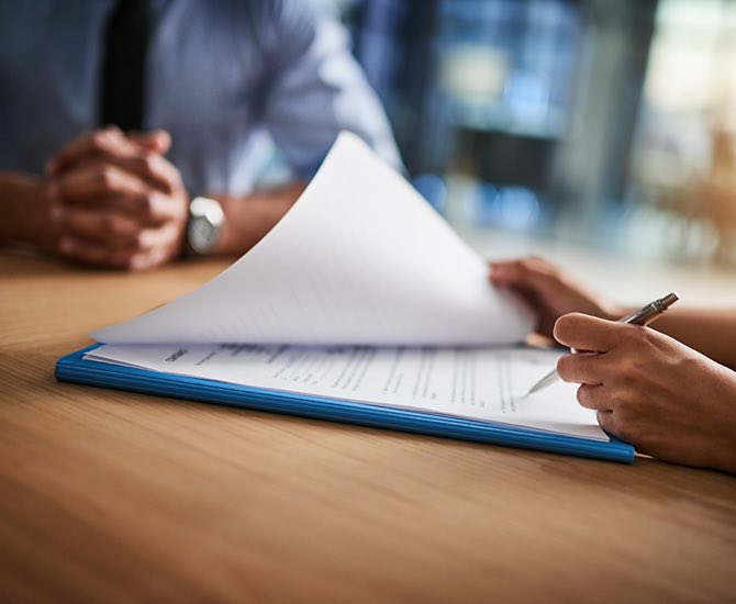 person looking over and preparing to sign a form with a man across the table