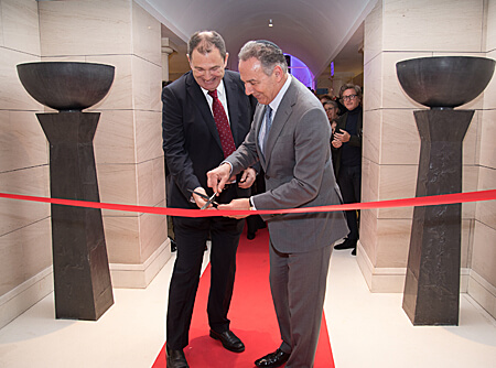 two men cutting red ribbon with scissors
