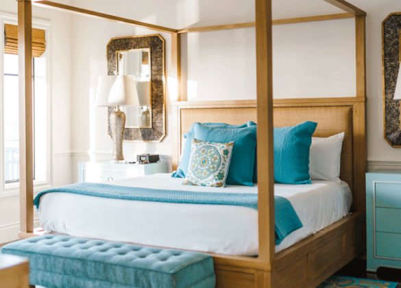 Wooden canopy bed with white linens and blue bench and colorful rug