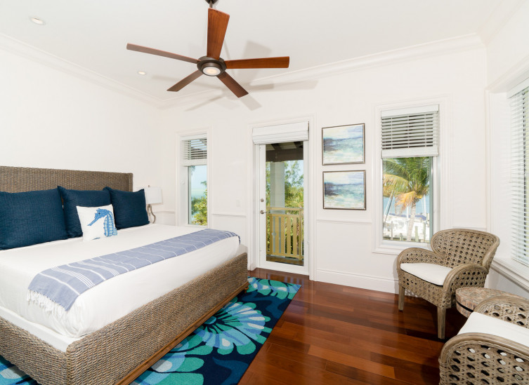 Room with king wicker bed frame, coral design rug & door to balcony