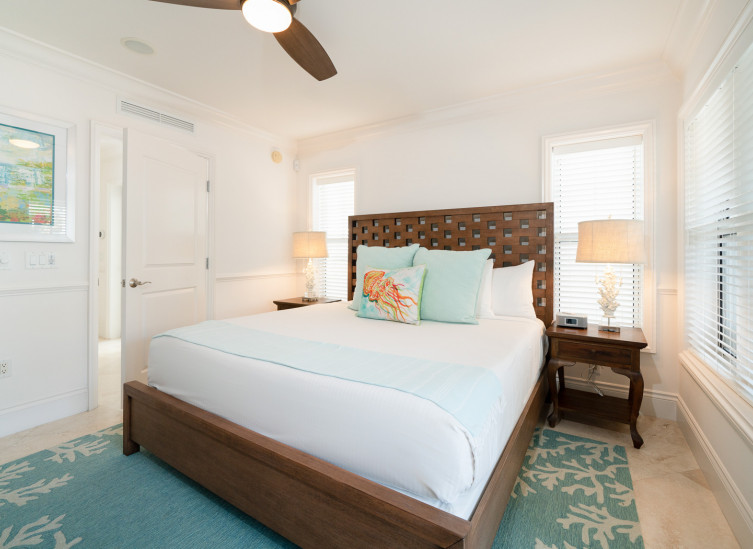 Room with double bed, wooden bed frame, sea themes rug & accent throw pillows