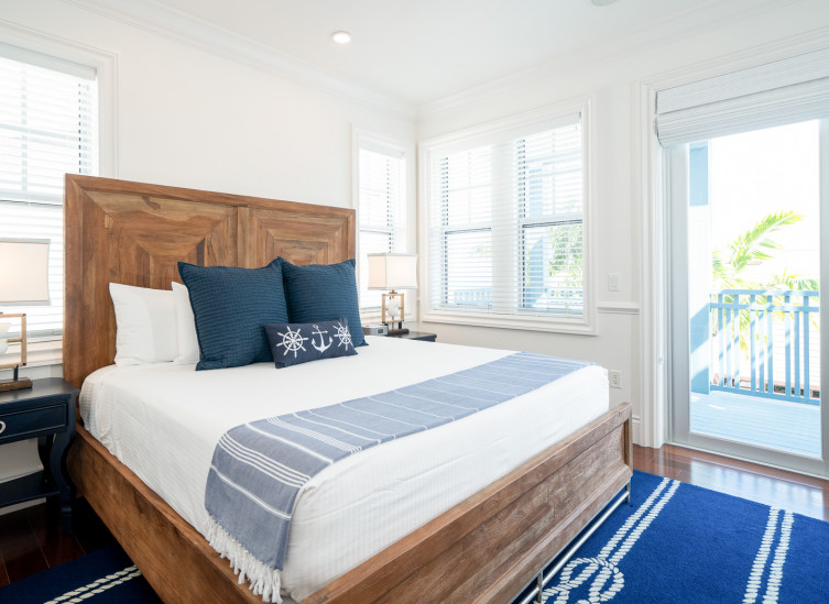 Room with double bed, wooden bed frame, dark blue rug & door leading to balcony