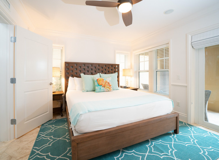 Room with king bed, wooden bed frame, aqua rug & door leading to balcony