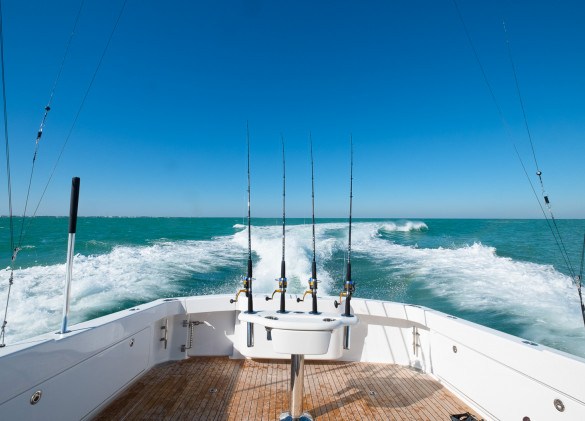 rear deck of a fishing boat with fishing poles looking out at the wake and blue green ocean