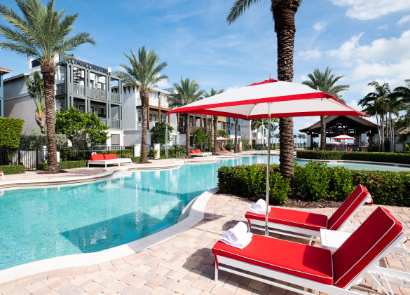 red chaise lounge and red and white umbrella on stone patio next to crystal blue pool