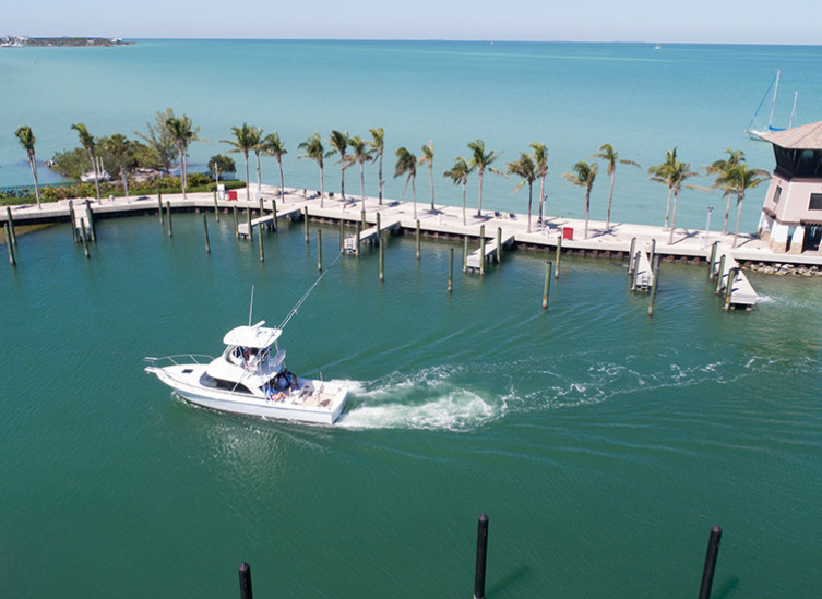 white boat cruising into marina with slips and ocean in background