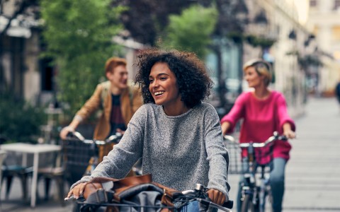 A group of friends smiling and riding bicycles on the sidewalk.