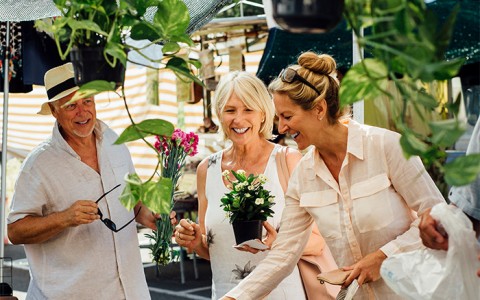 A woman looking down at plants with two friends smiling.
