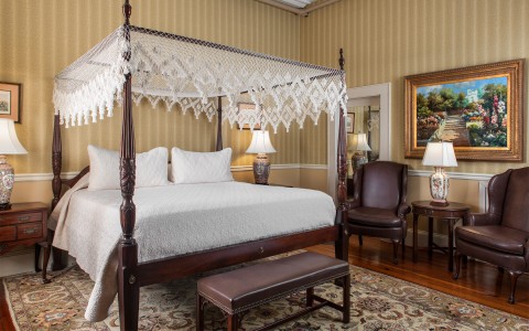 A large canopy bed and dark wood furniture in a room with striped wallpaper.