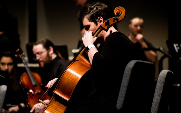 Concert Cellist dressed in black with the rest of the ensemble in the background