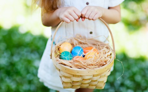 little girl in her sunday best holding a easter egg basket in the grass