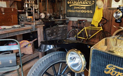 Museum of American Heritage room filled with dusted antiques from cars to chairs.